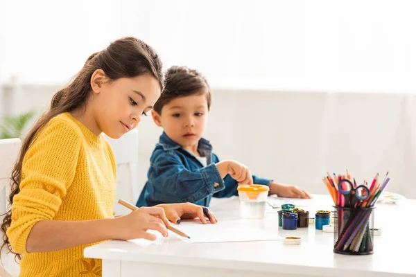 Enfoque selectivo de chico lindo mirando el dibujo de la hermana con lápiz - foto de stock