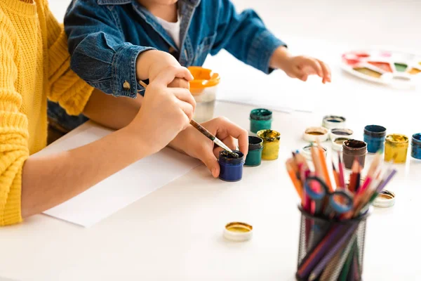 Vue recadrée du frère et de la sœur assis à table et dessinant avec des peintures ensemble — Photo de stock