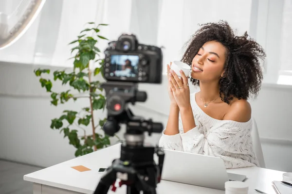 Selective focus of happy african american influencer in braces holding container with cosmetic cream near digital camera — Stock Photo