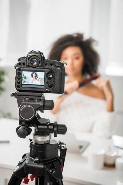 Enfoque selectivo de la cámara digital con rizado afroamericano influencer utilizando plancha de pelo en la pantalla — Stock Photo