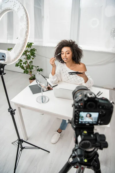 Foco seletivo de jovens afro-americanos influencer em aparelhos aplicando maquiagem perto da câmera digital — Fotografia de Stock