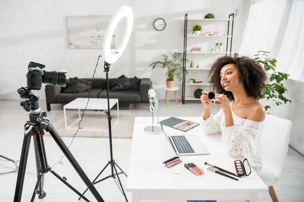 Щасливий афроамериканський відео блогер в брекетах, що тримає косметичний пензлик біля цифрової камери — стокове фото