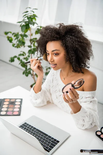 Frisée afro-américaine fille appliquant des cosmétiques décoratifs près d'un ordinateur portable — Photo de stock
