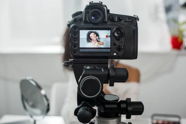 Foco seletivo da câmera digital com feliz blogueiro de vídeo afro-americano em aparelho com gloss labial e pincéis cosméticos em exibição — Fotografia de Stock