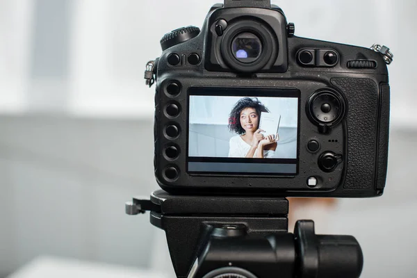 Selective focus of digital camera with african american video blogger holding notebook with influencer marketing lettering on display — Stock Photo