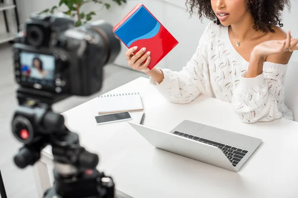 Ausgeschnittene Ansicht eines afrikanisch-amerikanischen Influencers, der eine bunte Schachtel in der Nähe der Digitalkamera hält — Stockfoto