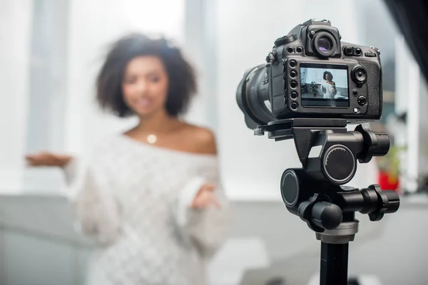 Messa a fuoco selettiva della fotocamera digitale con attraente afro-americano influencer gesticolare mentre si parla in mostra — Foto stock