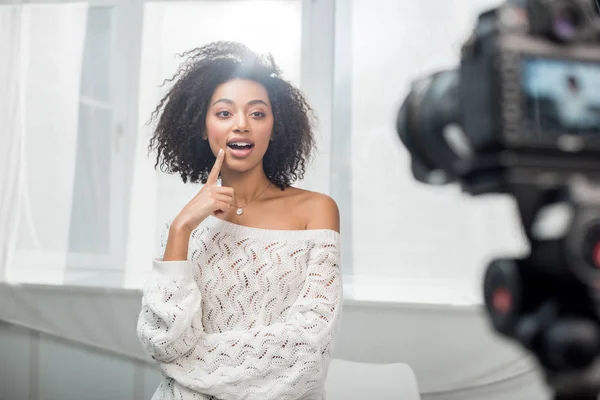 Selektiver Fokus der überraschten afrikanisch-amerikanischen Influencerin in Zahnspange, die das Gesicht in der Nähe der Digitalkamera berührt — Stockfoto