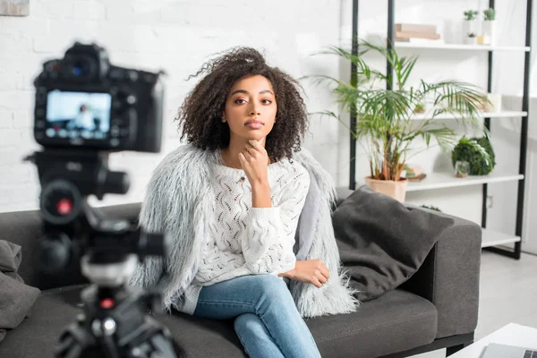 Messa a fuoco selettiva di bella influencer afro-americano guardando la fotocamera digitale mentre seduto sul divano — Foto stock