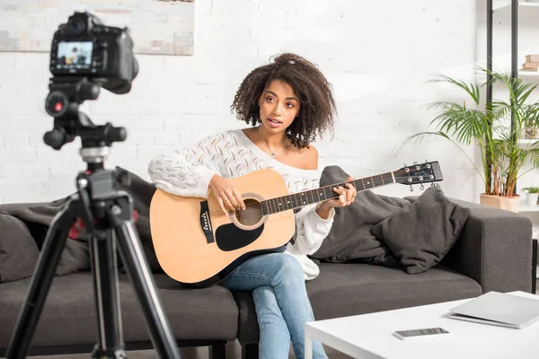 Selektiver Fokus der schönen afrikanisch-amerikanischen Influencerin, die Akustikgitarre in der Nähe der Digitalkamera spielt — Stockfoto