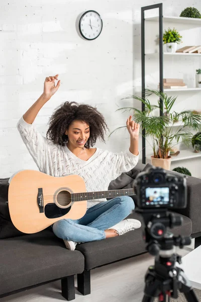 Selective focus of happy african american girl in braces gesturing near acoustic guitar and digital camera — Stock Photo