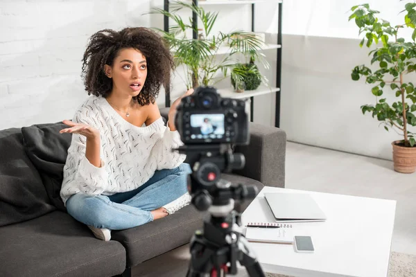 Selective focus of curly african american influencer in braces gesturing and talking near digital camera in living room — Stock Photo