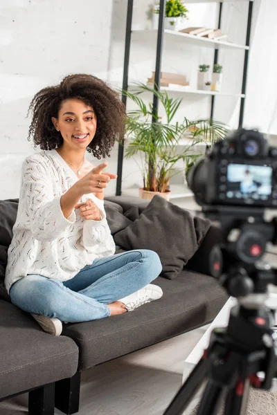Selective focus of happy african american influencer in braces pointing with finger at digital camera — Stock Photo