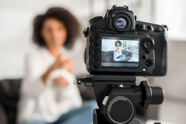 Selective focus of digital camera with happy african american influencer in braces pointing with finger on display — Stock Photo