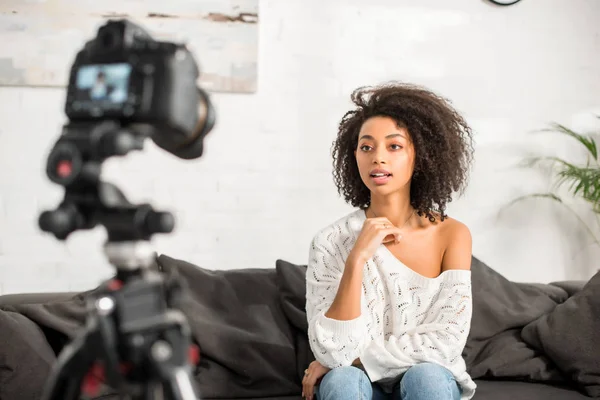 Messa a fuoco selettiva di giovane e riccia ragazza africana americana in apparecchio acustico parlando vicino alla fotocamera digitale — Foto stock