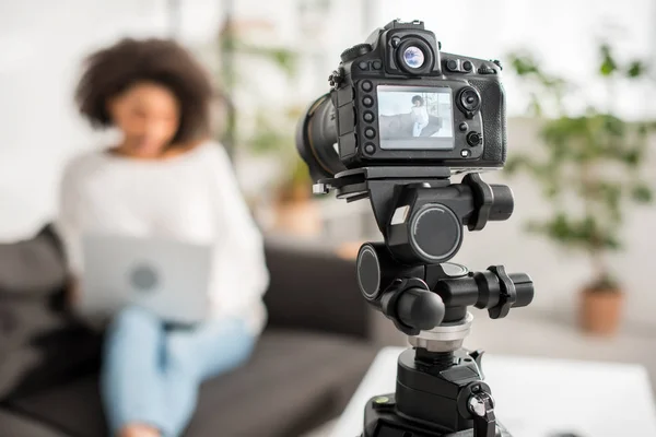 Foco seletivo da câmera digital com jovem blogueiro de vídeo afro-americano usando laptop em exibição — Fotografia de Stock