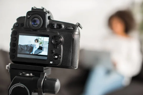 Selective focus of digital camera with african american video blogger using laptop near credit card on display — Stock Photo