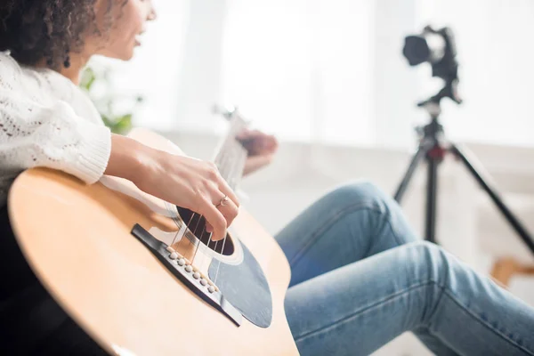Cropped view of young african american girl playing acoustic guitar near digital camera — Stock Photo