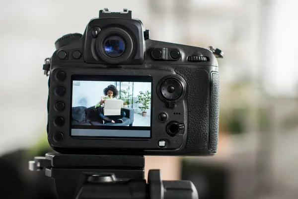 Selective focus of digital camera with sportive african american influencer opening carton box on display — Stock Photo