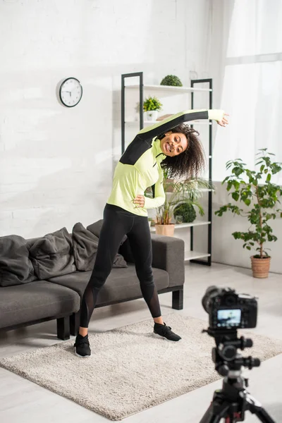 Selective focus of sportive african american video blogger in braces exercising near digital camera — Stock Photo