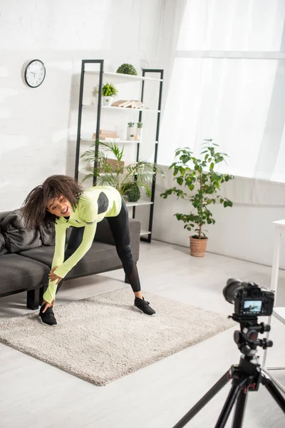 Selective focus of happy african american video blogger in braces exercising near digital camera — Stock Photo