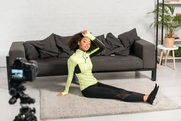 Foyer sélectif de blogueur vidéo afro-américain fatigué dans les bretelles reposant sur le tapis près de l'appareil photo numérique — Photo de stock