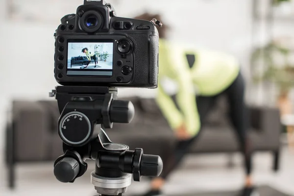 Foco seletivo da câmera digital com curly blogueiro de vídeo americano africano em aparelho exercendo em exibição — Fotografia de Stock
