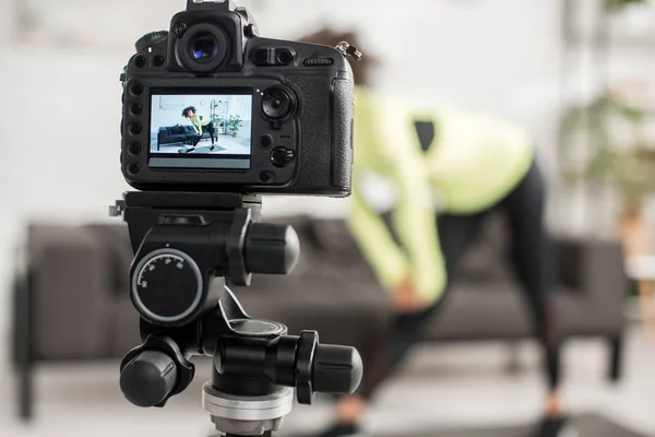 Selective focus of digital camera with curly african american video blogger in braces exercising on display — Stock Photo