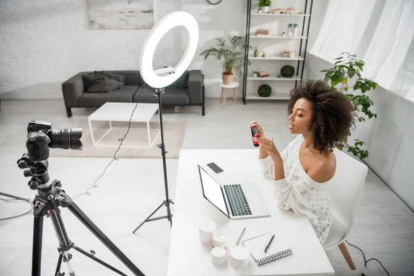 Afroamericano influencer celebración plancha de pelo cerca de cámara digital y portátil con pantalla blanca - foto de stock