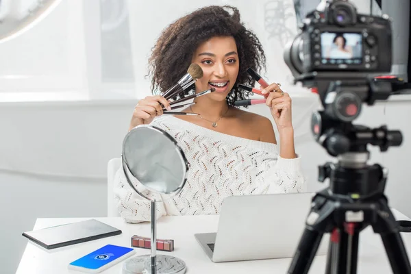 KYIV, UCRAINA - 10 DICEMBRE 2019: focus selettivo della ragazza afroamericana in bretelle con lucidalabbra e pennelli cosmetici vicino allo smartphone con app shazam — Foto stock