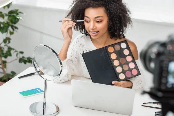 KYIV, UKRAINE - DECEMBER 10, 2019: selective focus of african american influencer in braces applying eye shadow near smartphone with twitter app on screen — Stock Photo