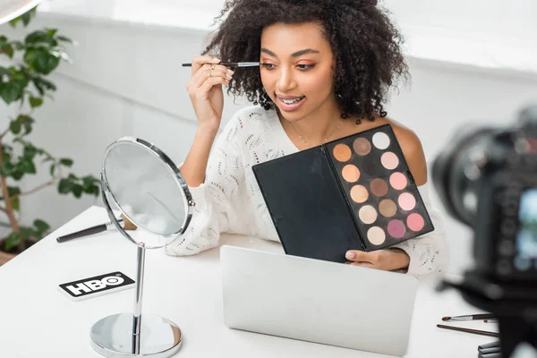 KYIV, UKRAINE - DECEMBER 10, 2019: selective focus of african american influencer in braces applying eye shadow near smartphone with hbo app on screen — Stock Photo