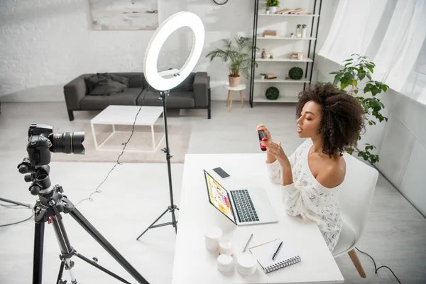 KYIV, UCRANIA - 10 DE DICIEMBRE DE 2019: Afroamericano influencer holding hair straightener near digital camera and laptop with aliexpress website - foto de stock