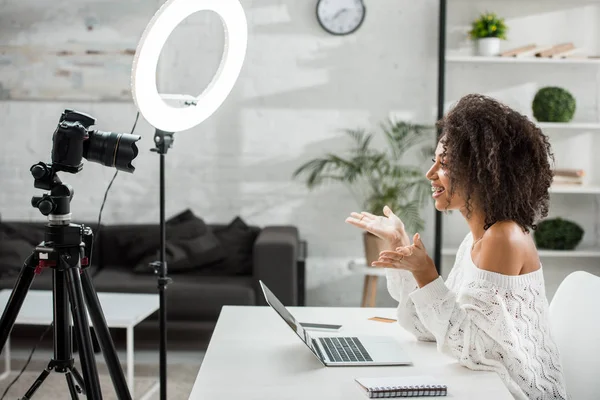 Side view of happy african american influencer in braces gesturing near digital camera — Stock Photo