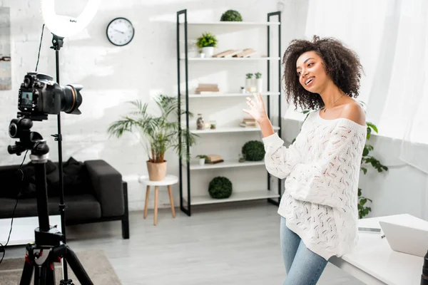 Cheerful african american influencer in braces waving hand near digital camera — Stock Photo