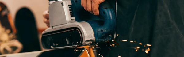 Panoramic shot of worker repairing ski with belt sander in repair shop — Stock Photo