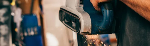 Panoramic shot of worker repairing ski with belt sander in repair shop — Stock Photo