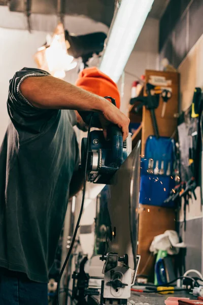 Worker repairing snowboard with belt sander in repair shop — Stock Photo