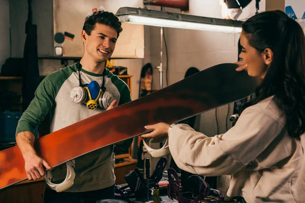 Femme donnant snowboard au travailleur souriant dans l'atelier de réparation — Photo de stock