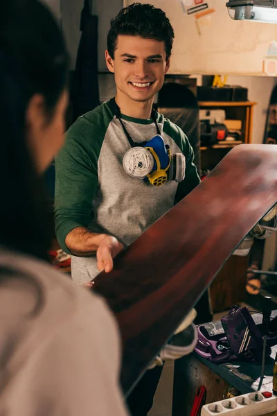 Cropped view of woman giving snowboard to smiling worker in repair shop — Stock Photo