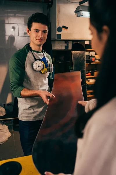 Cropped view of woman giving snowboard to worker in repair shop — Stock Photo
