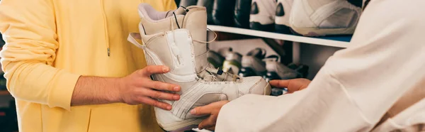 Panoramic shot of worker showing ski boot to client in repair shop — Stock Photo
