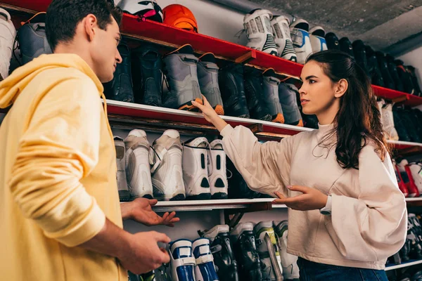 Low angle view of worker holding ski boot and talking with client in repair shop — Stock Photo