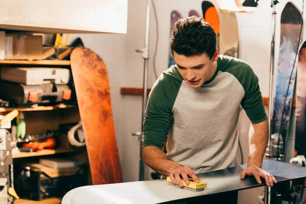 Schöner Arbeiter mit Pinsel auf Snowboard in Reparaturwerkstatt — Stockfoto