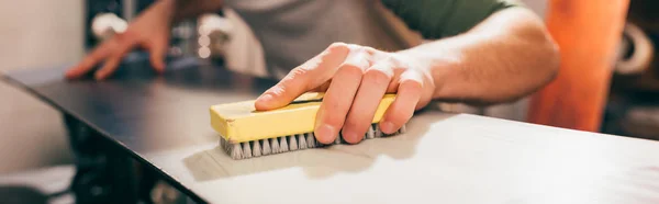 Panoramic shot of worker using brush on snowboard in repair shop — Stock Photo