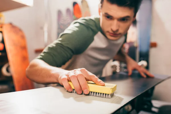 Messa a fuoco selettiva del lavoratore utilizzando pennello su snowboard in officina di riparazione — Foto stock