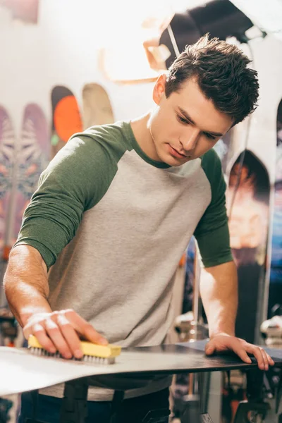 Beau travailleur utilisant brosse sur snowboard dans l'atelier de réparation — Photo de stock