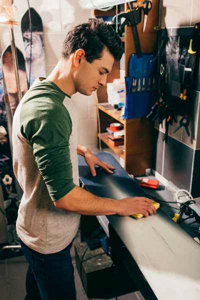 Side view of worker using brush on snowboard in repair shop — Stock Photo