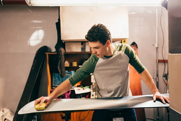 Handsome worker using brush on snowboard in repair shop — Stock Photo