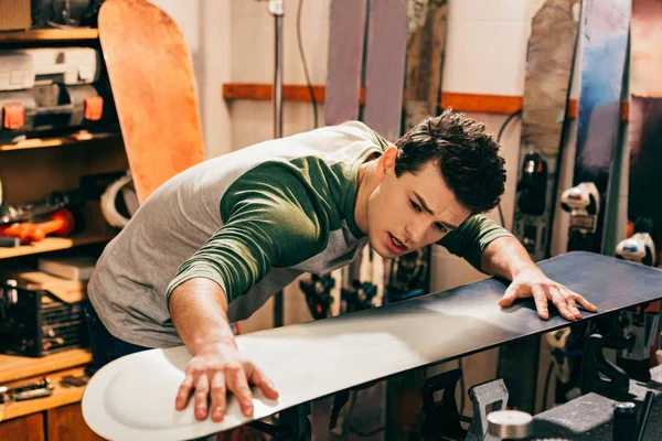 Handsome worker touching snowboard in repair shop — Stock Photo